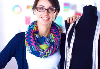 Fashion designer posing with a black dress form with many tape measures hanging around the dress form's neck