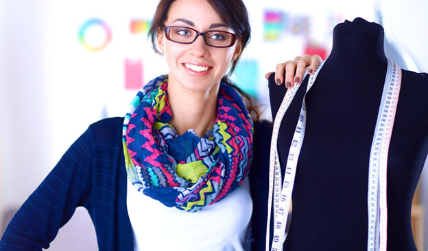 Fashion designer posing with a black dress form with many tape measures hanging around the dress form's neck